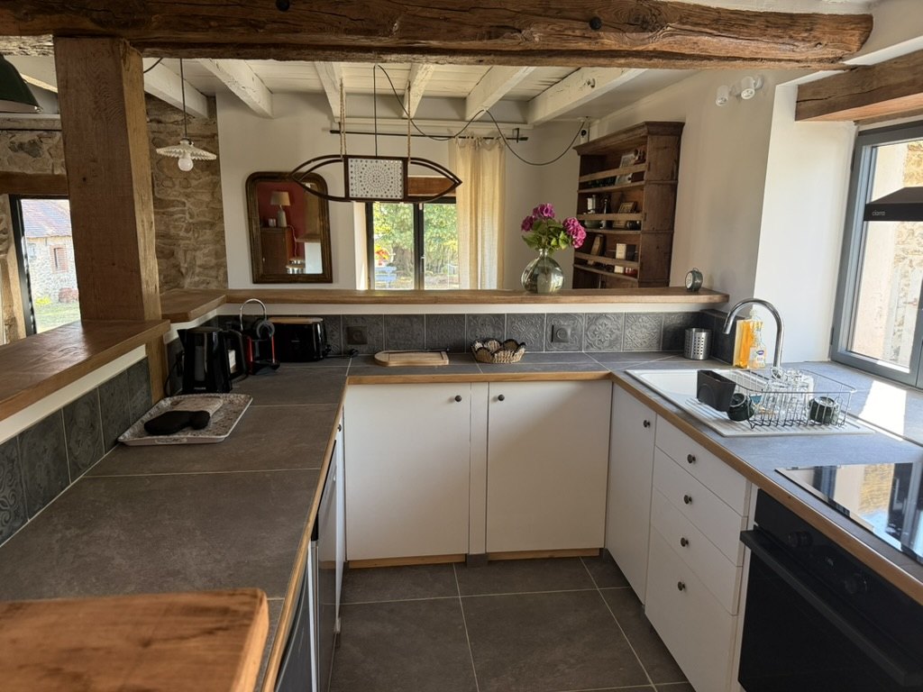 La Bergerie's kitchen: U-shaped worktop, induction hob, oven, sink under the window, oak bar and an antique dresser at the back