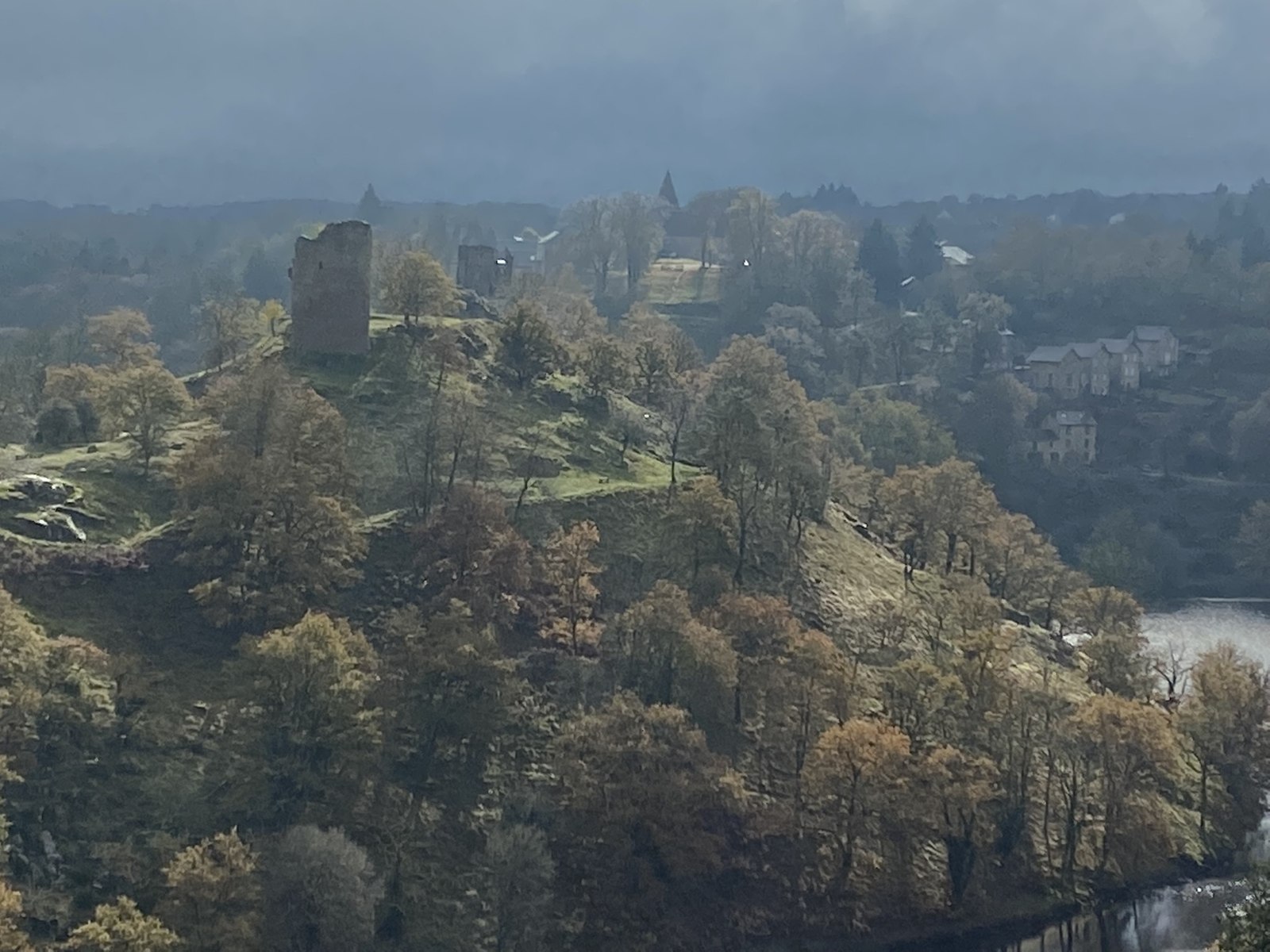 Depuis le rocher de la Fileuse : le donjon de la forteresse de Crozant sur son éperon boisé, le village derrière, la Creuse en contrebas, dans la brume d'automne