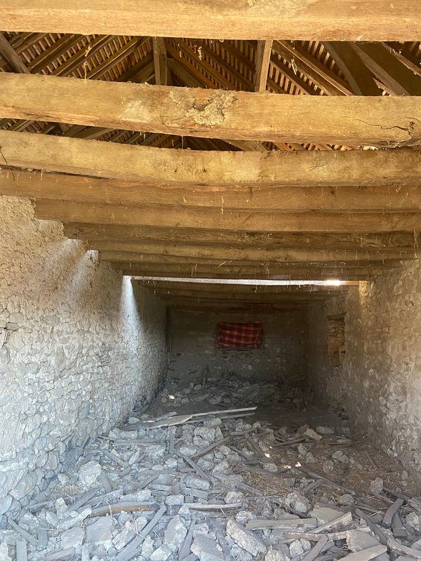 Charpente et murs en pierre vus de l’intérieur avant travaux, gravats au sol